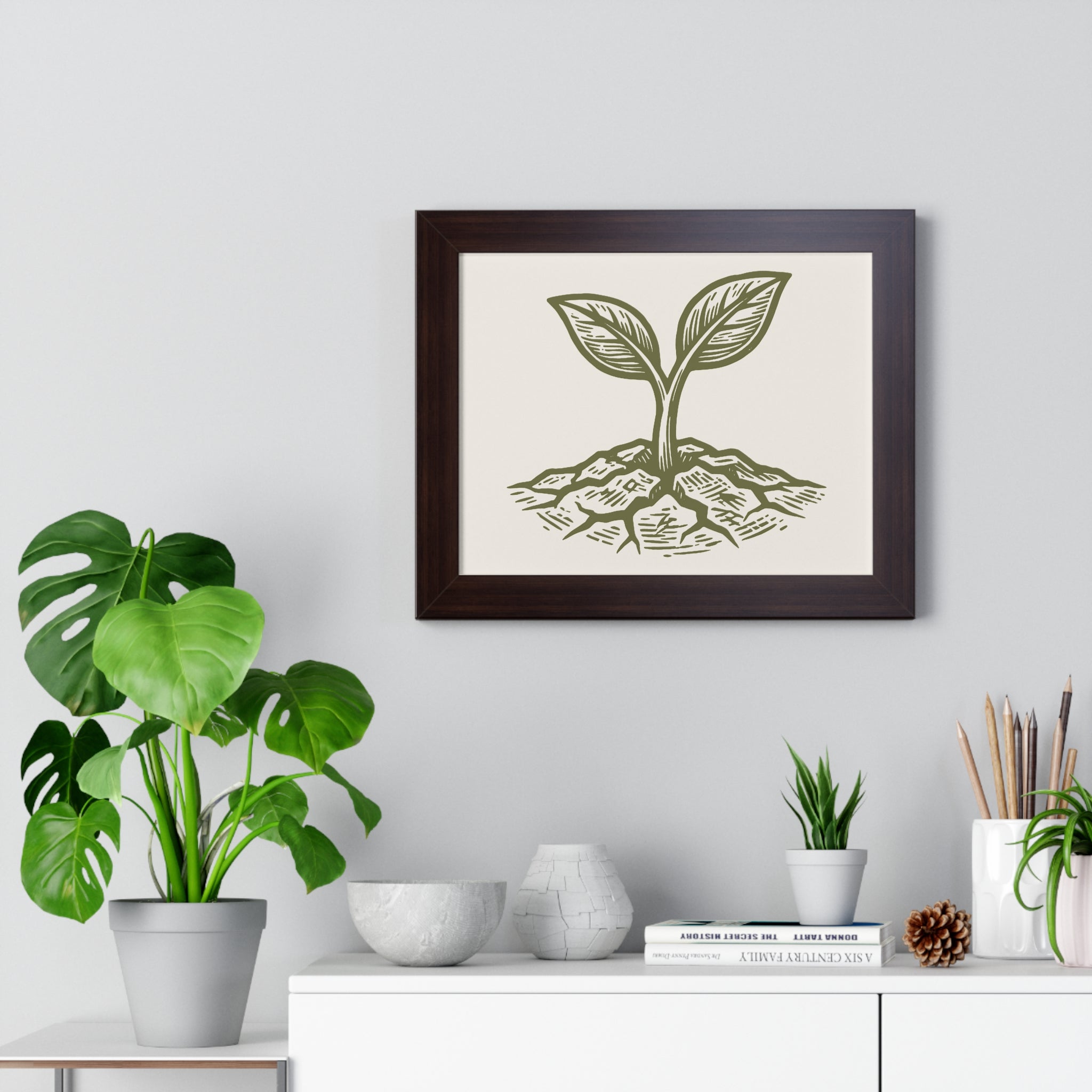The Original Framed Poster in Walnut hanging on a gray wall above a shelf with houseplants, featuring an etching-style sprouting seed illustration on a Parchment background