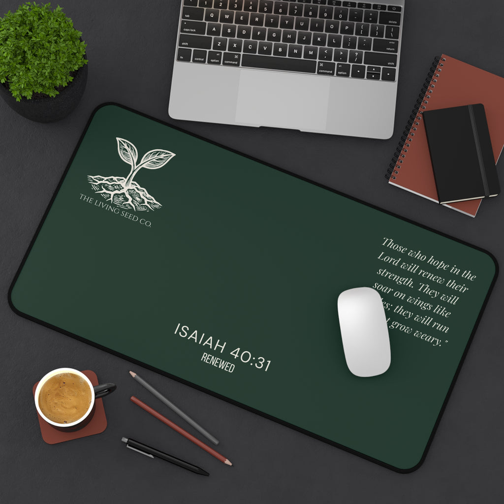 Scripture Series RENEWED Desk Mat in Forest Deep 12x22 — lifestyle shot — forest green desk mat on a dark workspace with laptop, coffee, and stationery featuring The Living Seed Co. seedling logo, Isaiah 40:31, RENEWED wordmark, and full Isaiah 40:31 verse in parchment ink.