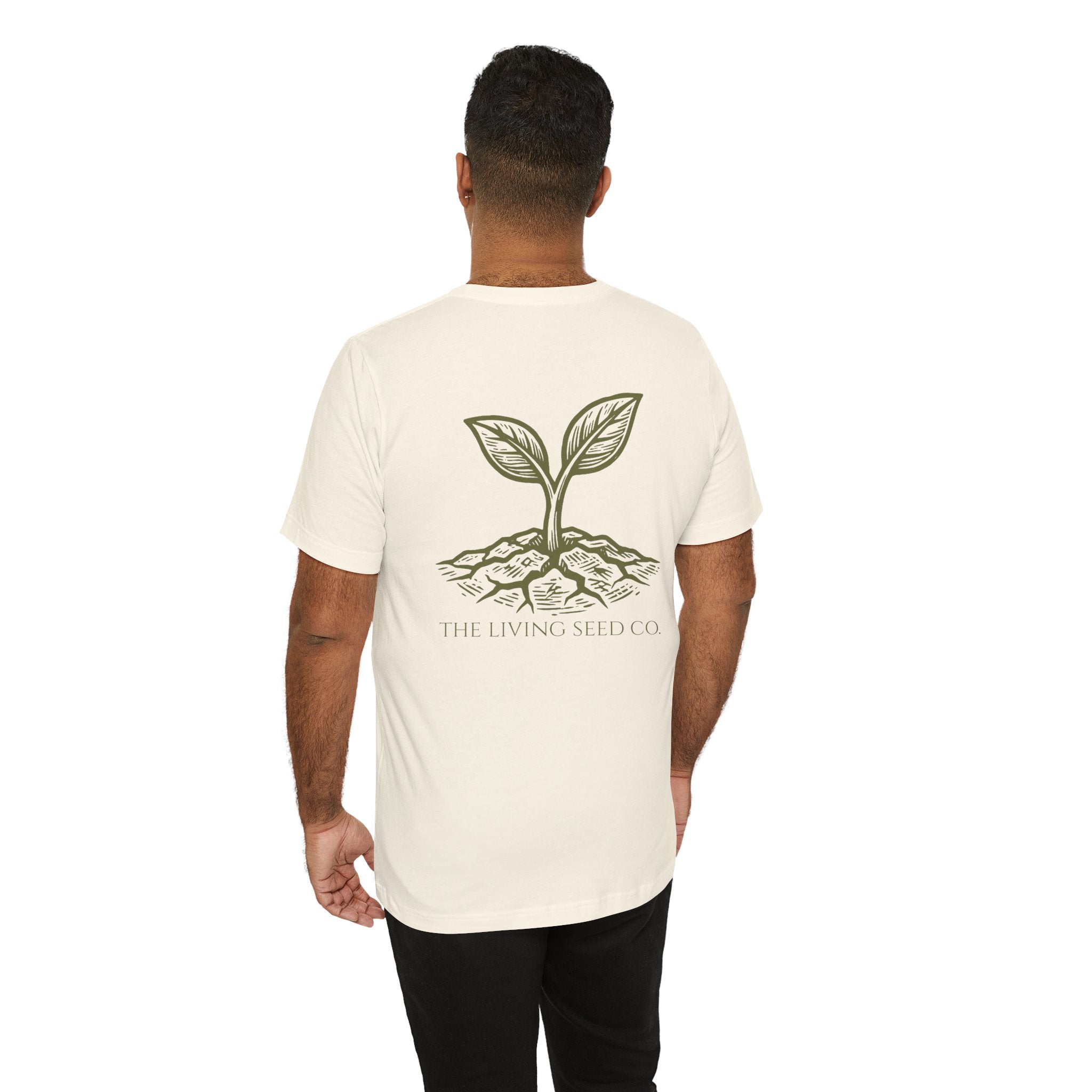 The Original Tee in Natural — back view — man wearing cream unisex t-shirt featuring The Living Seed Co. etching-style sprouting seed graphic in olive ink with wordmark below. Bella+Canvas 3001.