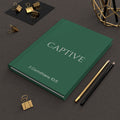 Scripture Series CAPTIVE Journal in Garden Green — lifestyle shot — garden green hardcover journal featuring CAPTIVE in parchment lettering with 2 Corinthians 10:5 reference, styled on a desk with gold stationery accessories.