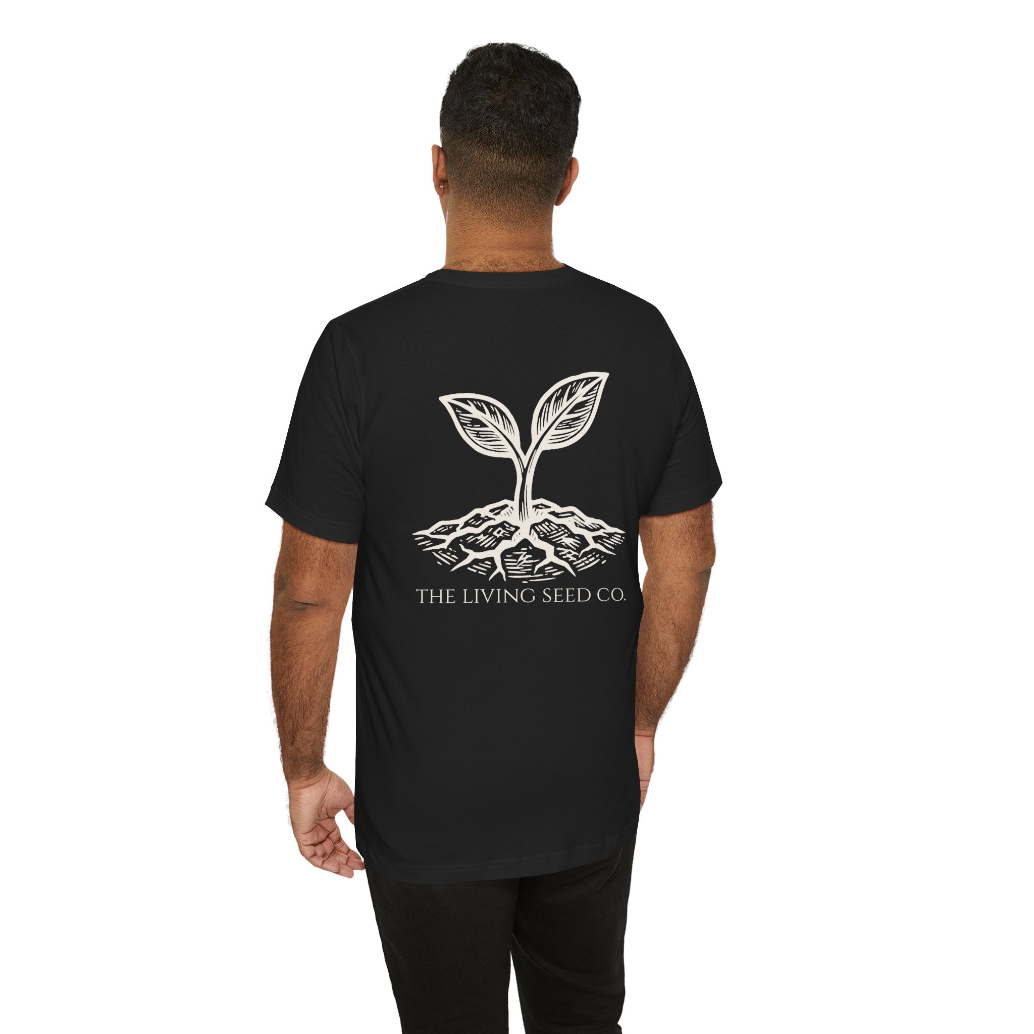 The Original Tee in Black — back view — man wearing black unisex t-shirt featuring The Living Seed Co. etching-style sprouting seed graphic in parchment ink with wordmark below. Bella+Canvas 3001.