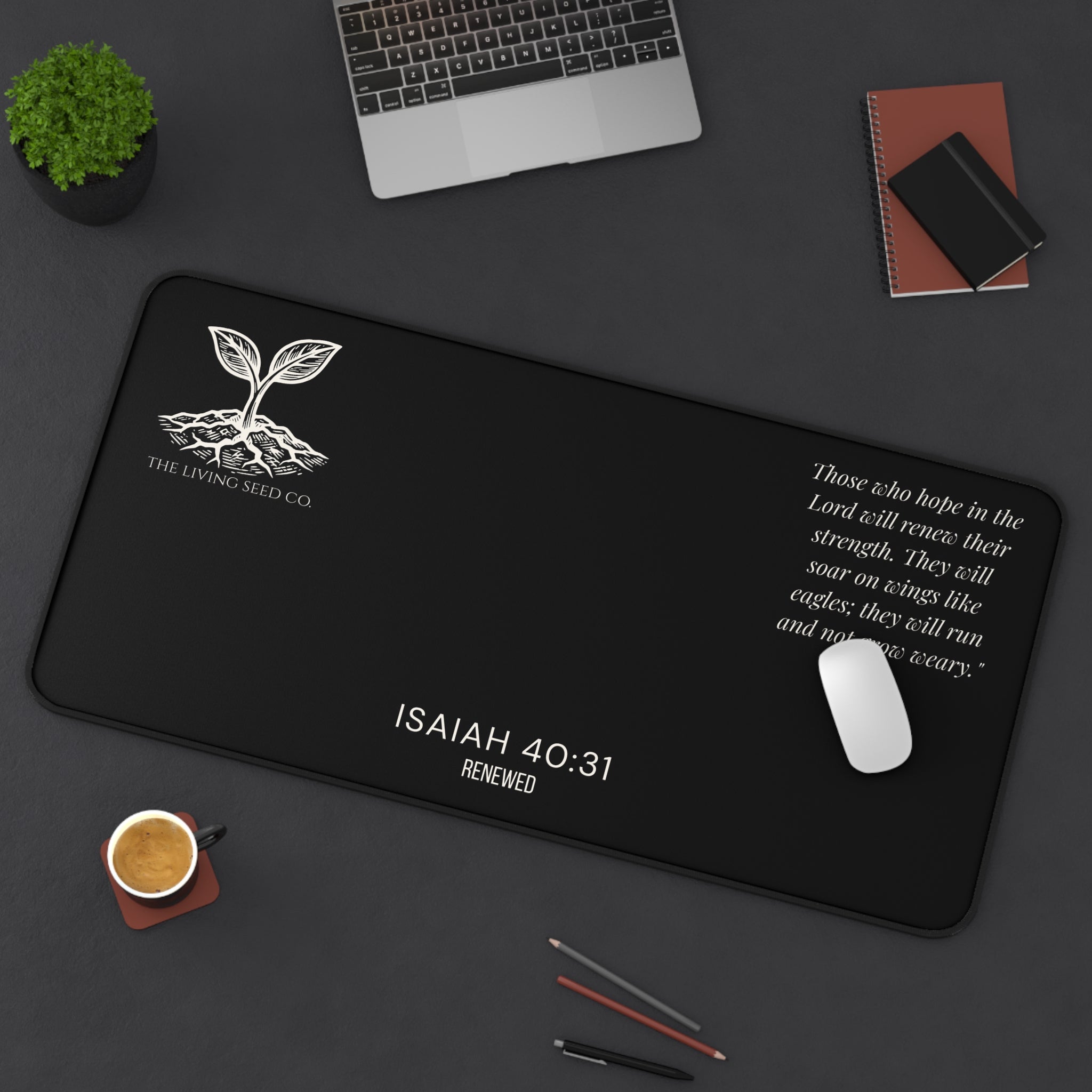 Scripture Series RENEWED Desk Mat in Black 16x32 — lifestyle shot — forest green desk mat on a dark workspace with laptop, coffee, and stationery featuring The Living Seed Co. seedling logo, Isaiah 40:31, RENEWED wordmark, and full Isaiah 40:31 verse in parchment ink.