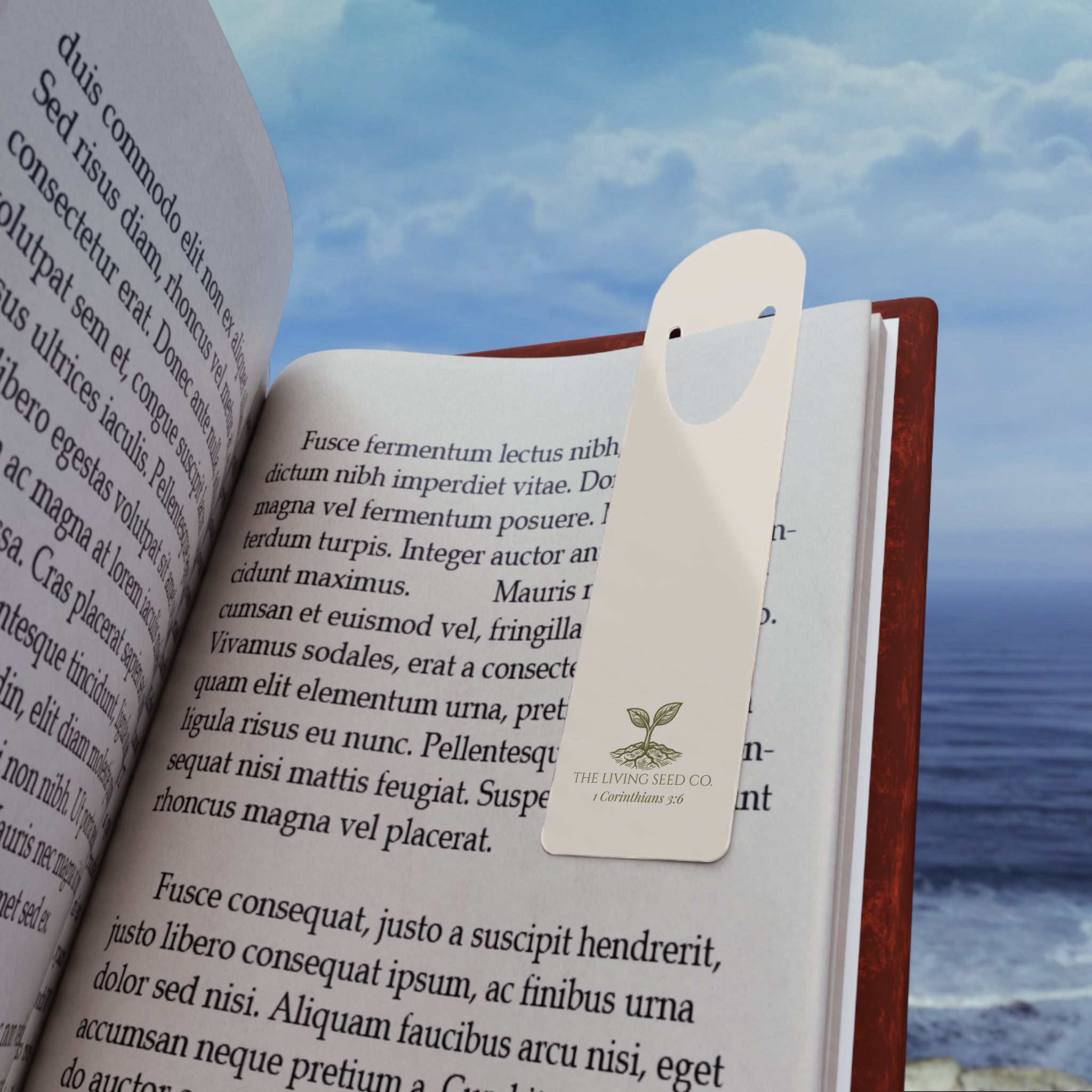 Parchment aluminum bookmark resting in an open book with an ocean view in the background, featuring The Living Seed Co. logo and 1 Corinthians 3:6