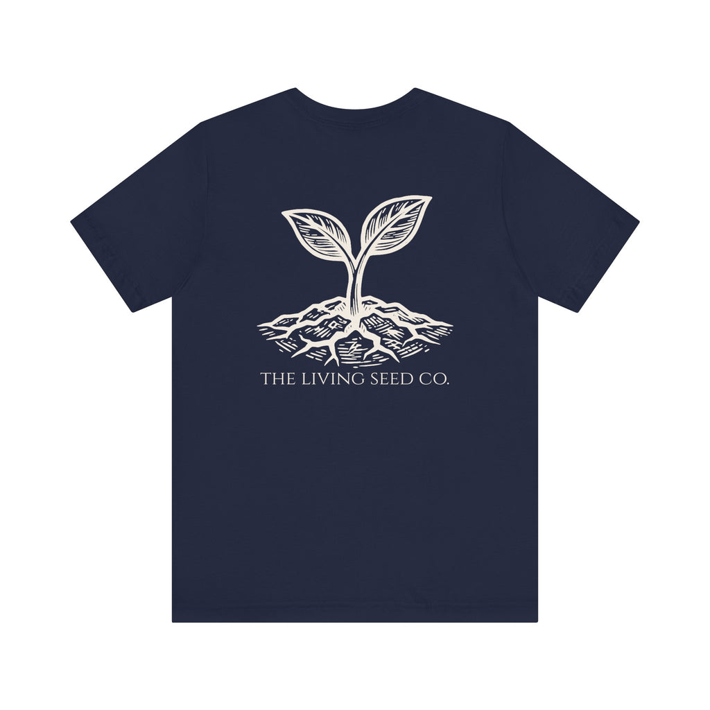 The Original Tee in Navy — back view flat mockup — navy unisex t-shirt featuring The Living Seed Co. etching-style sprouting seed graphic in parchment ink with wordmark below. Bella+Canvas 3001.