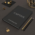 Scripture Series CAPTIVE Journal in Midnight Black — lifestyle shot — black hardcover journal featuring CAPTIVE in parchment lettering with 2 Corinthians 10:5 reference, styled on a desk with gold stationery accessories.