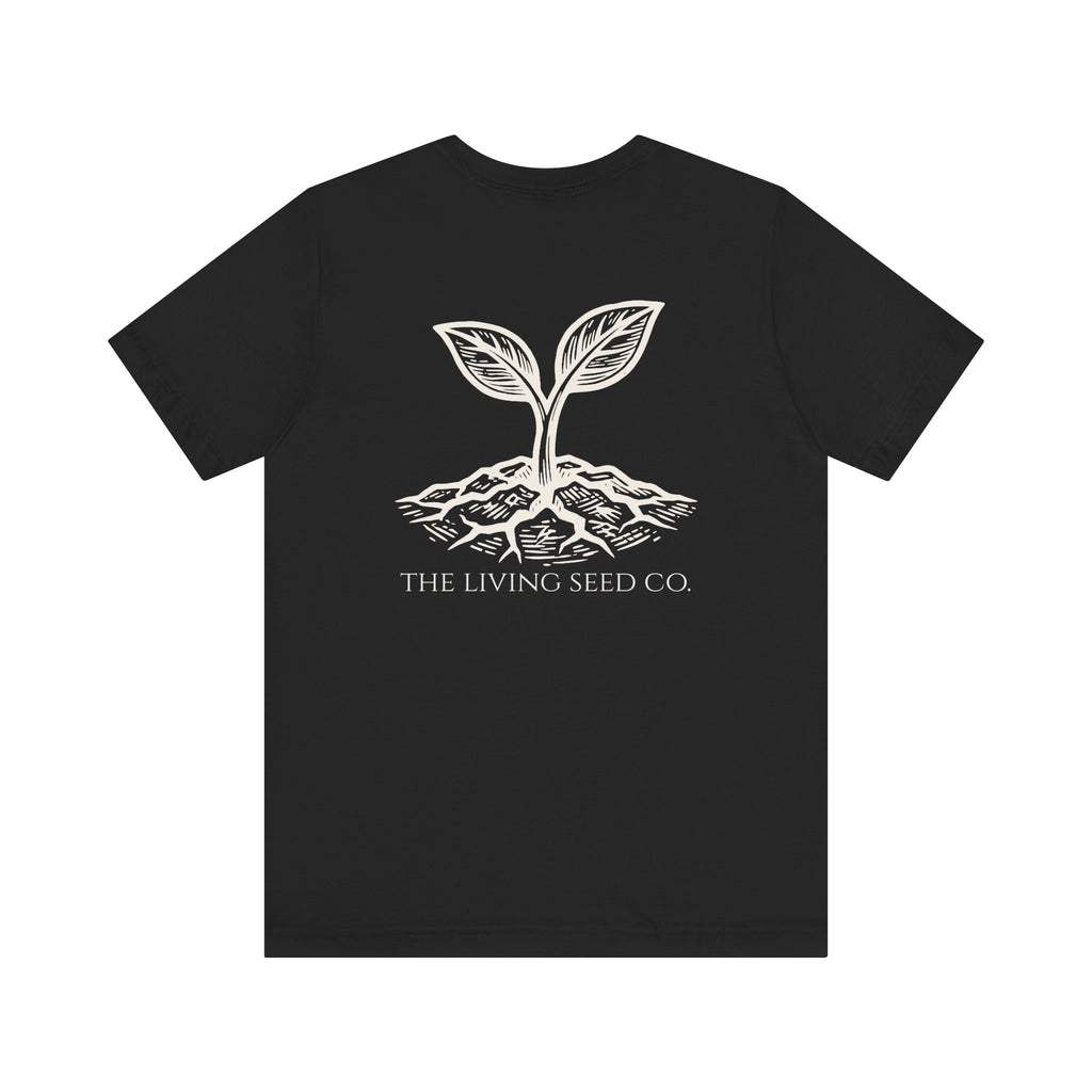 The Original Tee in Black — back view flat mockup — black unisex t-shirt featuring The Living Seed Co. etching-style sprouting seed graphic in parchment ink with wordmark below. Bella+Canvas 3001.
